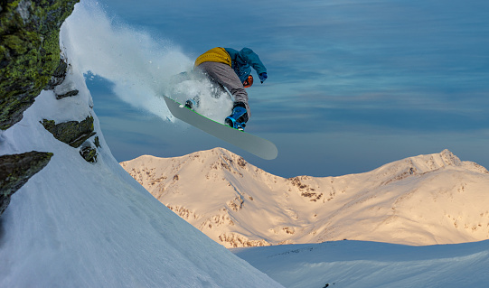 Snowboarder jumping mid air in beautiful mountain landscape at sunset