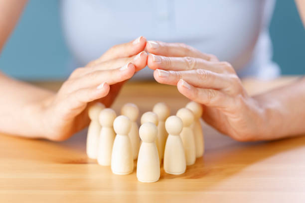 Close up shot of a woman hand guarded protect wooden people on table. Human resources, insurance, human health concepts stock photo
