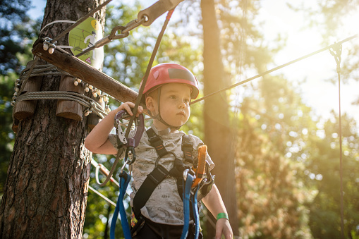 Cute little boy goes through an obstacle course in an adventure park at sunset
