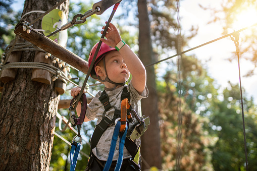 Cute little boy goes through an obstacle course in an adventure park at sunset