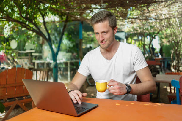 istock Young Man working with laptop outdoor in a beautiful terrace using smartphone and computer sitting cross-legged in Home work. 1406870606