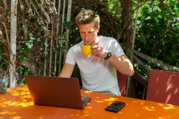 istock Young Man working with laptop outdoor in a beautiful terrace using smartphone and computer sitting cross-legged in Home work. 1406870888