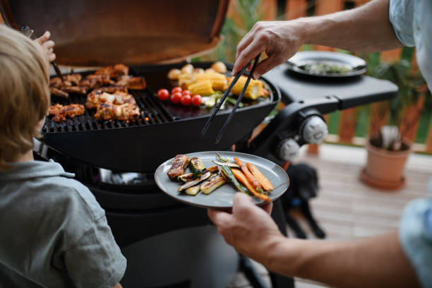 unkenntlicher vater mit kleinem sohn, der während der sommergartenparty der familie rippchen und gemüse auf dem grill grillt, nahaufnahme - child vegetable squash corn stock-fotos und bilder