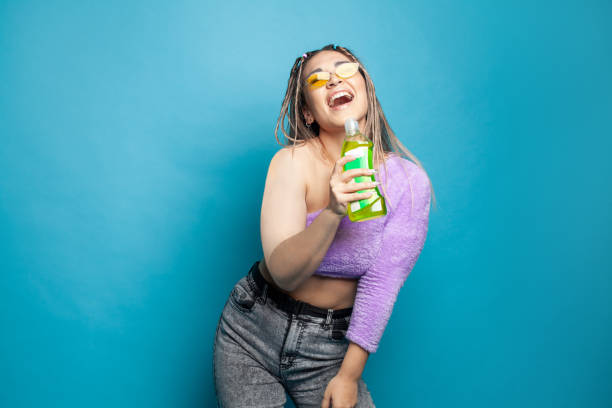 istock Pretty young woman singing with plastic bottle against blue studio wall background 1406871959