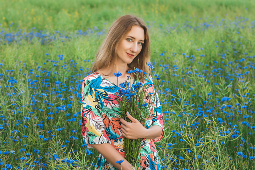 Young pretty woman among the field of beautiful cornflowers closeup
