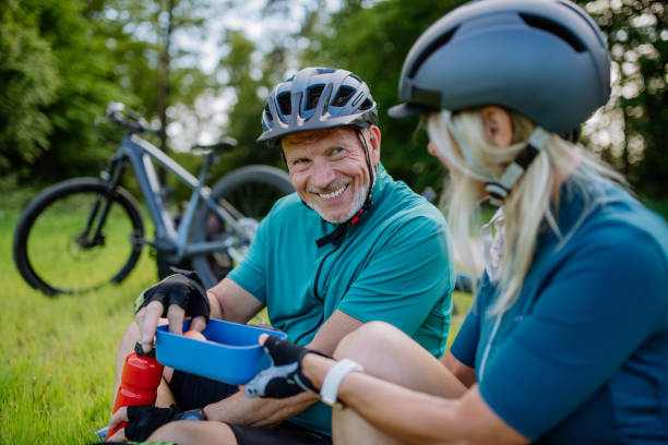 istock Active senior couple resting after bicycle ride at summer park, sitting on grass and having snack. 1406872148