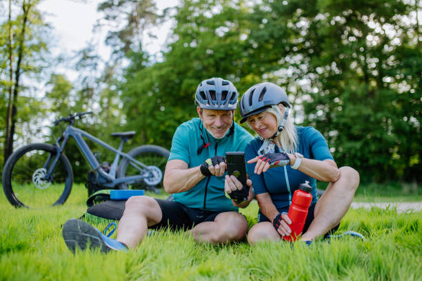 istock Active senior couple resting after bicycle ride at summer park, sitting on grass and using smartphone. 1406872218