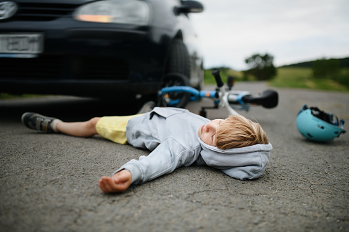 A little boy fallen from bicycle after car accident and helmet on road