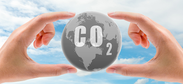 CO2 capture concept. Human hand holding CO2 in globe map on blue sky. Carbon capture and storage technology concept. Greenhouse gas. Carbon dioxide gas global air climate pollution. Environment issue.