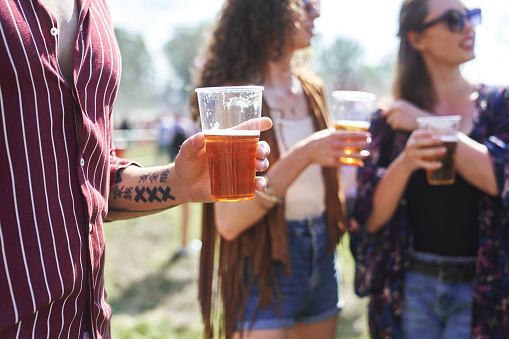 Part of man's hand holding glass of beer at music festival