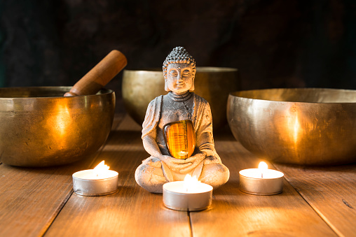 Still life with singing bowls, minerals, candles and a Buddha figure on wooden boards and a dark background. Small altar illuminated with small candles for meditation and music therapy.