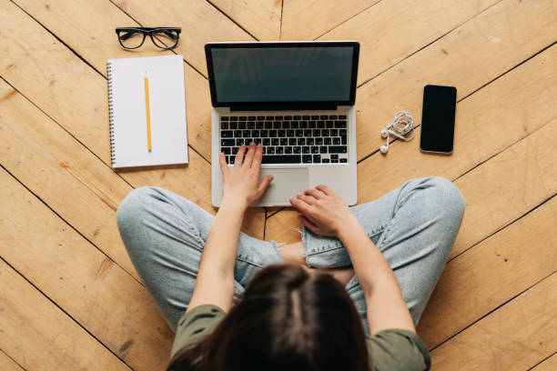 istock Top view of anonymous lady typing on keypad sitting on wooden floor with notebook and mobile 1406877310