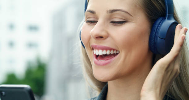 S001_C046_0101CI Copy retouch JBL logo primer plano de una mujer escuchando música con auriculares y un teléfono. mujer escribiendo en un teléfono celular con auriculares inalámbricos bluetooth. señora de pie afuera en la ciudad usando un teléfono inteligente seleccionando una canción