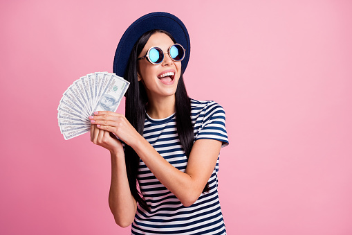 Photo portrait of excited woman with open mouth showing money fan isolated on pastel pink colored background.