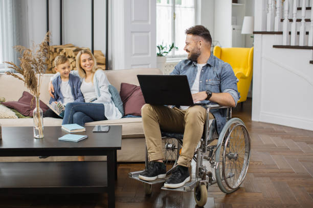 uomo disabile con laptop che guarda moglie e figlio a casa - two parent family technology mobility men foto e immagini stock