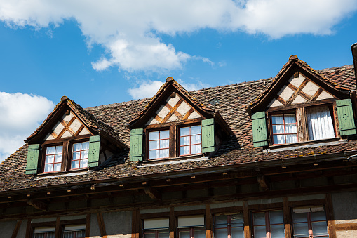 Old vintage European decorated attic windows with open wooden shutter and facade decoration in a small village in Switzerland. Cloudy blue sky in the background, no people.