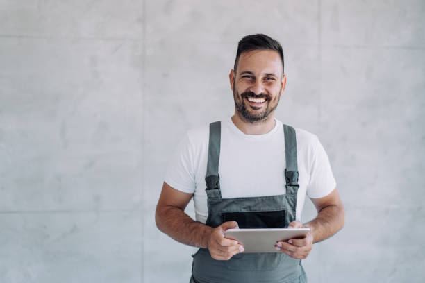 joven trabajador con uniforme general usando tabletas en su lugar de trabajo. - overalls fotografías e imágenes de stock