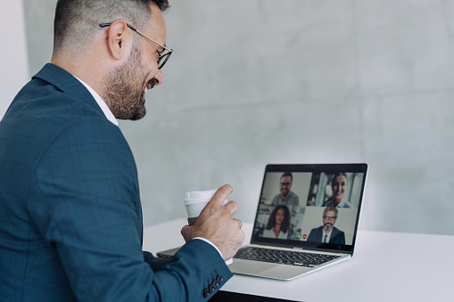 Businessman talking to his colleagues about business plan in video conference. Corporate business team using laptop for an online meeting in video call. Shot of unrecognizable businessman using a laptop for web conference.