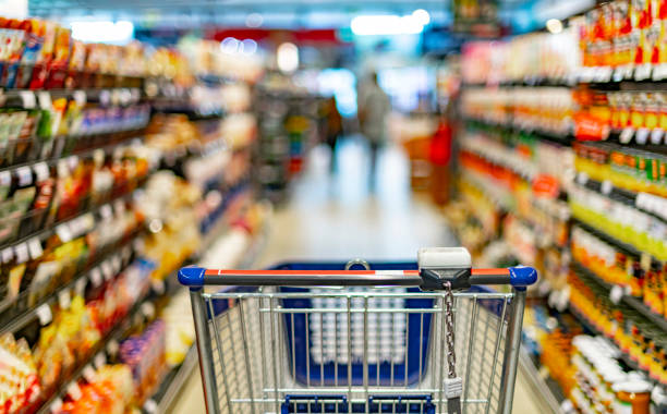 a shopping cart by a store shelf in a supermarket - supermarket imagens e fotografias de stock