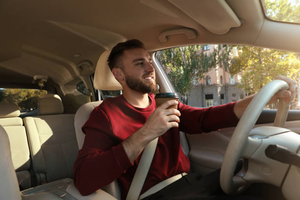 istock Handsome young driver with cup of drink sitting in modern car 1406887413
