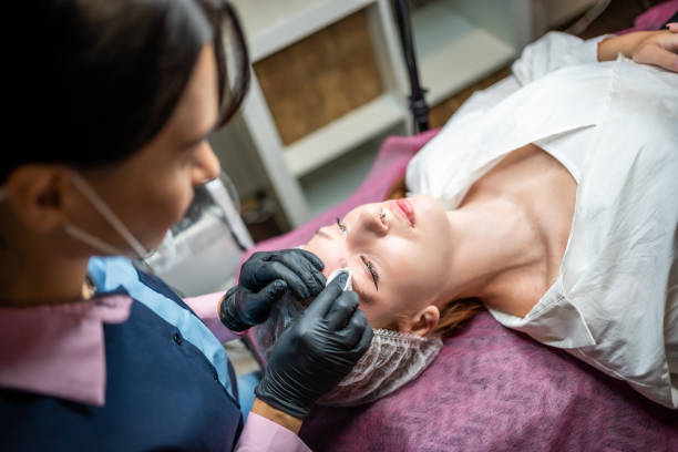 istock Permanent makeup artist prepares the client's face with the procedure, cleans the eyebrows from dirt and grease with a cotton pad. Eyebrow permanent makeup procedure, microblading. 1406887550