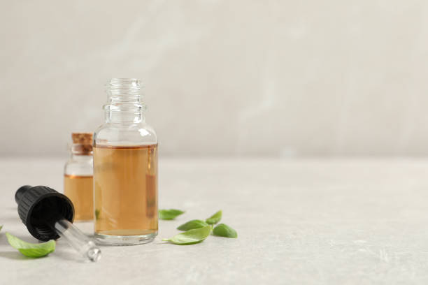 istock Bottles of essential basil oil and fresh leaves on light grey table, space for text 1406887822