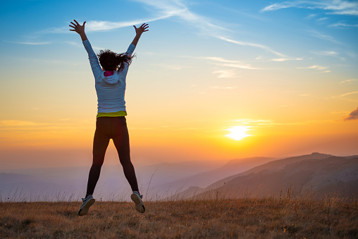 Young happy woman jumping at sunset mountains with sunset hills and mountain landscape