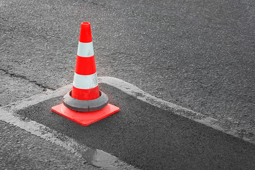 istock Patching of asphalt road. Striped orange and white reflective cone marks repair site 1406888816