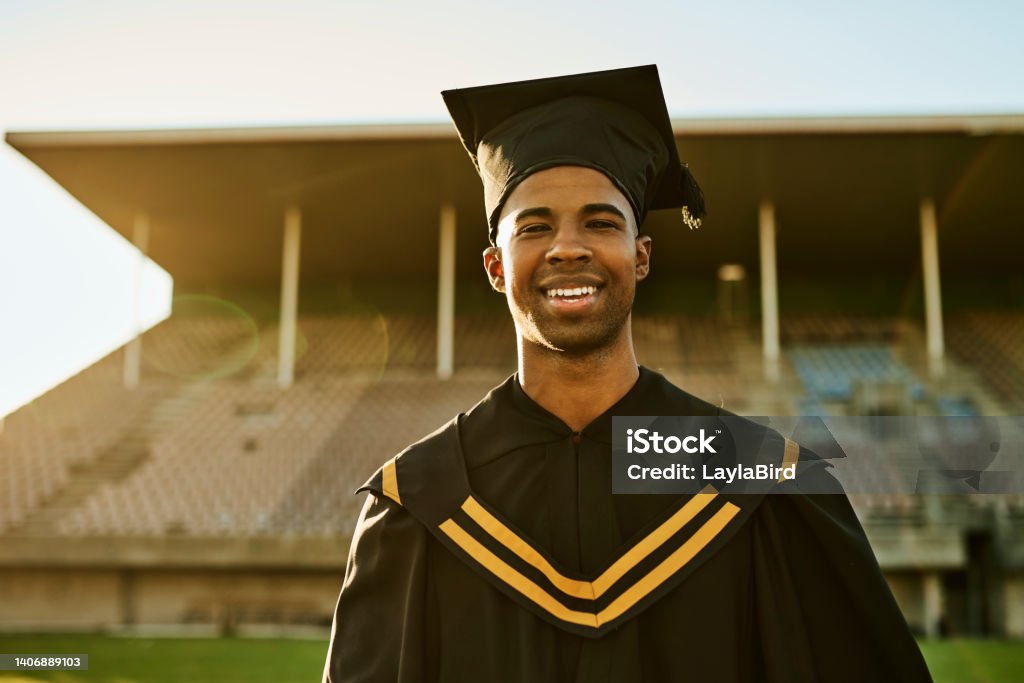 Portrait of smiling graduate in gown and hat standing alone on university campus at graduation ceremony. Excited, happy qualified postgrad graduating college for academic bachelor, masters and degree 20-24 Years Stock Photo