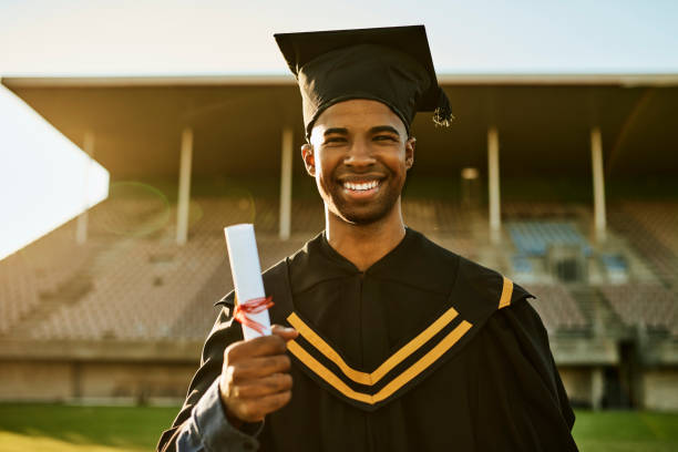 Portrait of smiling graduate in gown and hat standing alone on university campus at graduation ceremony. Excited, happy qualified postgrad graduating college for academic bachelor, masters and degree Portrait of smiling graduate in gown and hat standing alone on university campus at graduation ceremony. Excited, happy qualified postgrad graduating college for academic bachelor, masters and degree Master’s Degree stock pictures, royalty-free photos & images