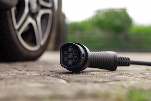 Still life of a car charger on the floor outside next to an electric car.