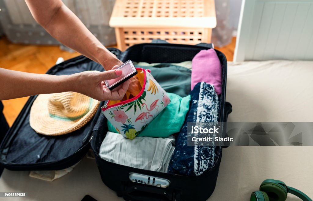 Packing suitcase for travel Close up of females hands packing suitcase  for summer vacation. Suitcase is on the bed  in bedroom. Packing make-up in a make-up  bag. Make-Up Bag Stock Photo