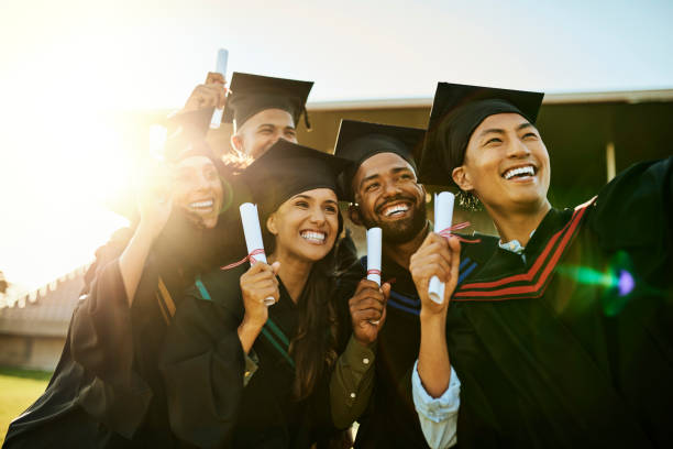 étudiants qualifiés le jour de la remise des diplômes. groupe d’élèves en robe prenant un selfie avec téléphone lors de la cérémonie. des diplômés motivés qui prennent des photos mémorables, célèbrent la réussite scolaire et les jalons - remise de diplôme photos et images de collection