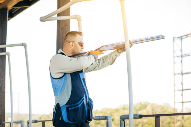 erwachsener mann mit sonnenbrille und gewehrweste, der das schießen mit feuerwaffen übt. junge erfahrene männliche zielschrotflinte im freien. - sport clipping path handgun pistol stock-fotos und bilder