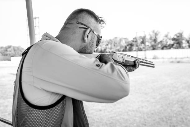 erwachsener mann mit sonnenbrille und gewehrweste, der das schießen mit feuerwaffen übt. junge erfahrene männliche zielschrotflinte im freien. - sport clipping path handgun pistol stock-fotos und bilder