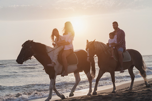 The family spends time with their children while riding horses together on a sandy beach. Selective focus . High quality photo