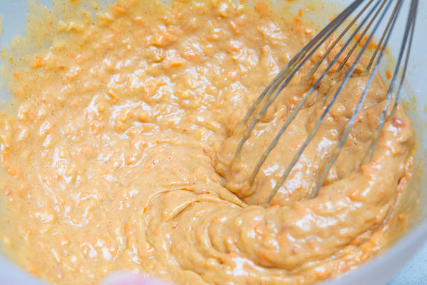 Mixing a carrot cake in a plastic bowl, Mixing it with wire whisks,