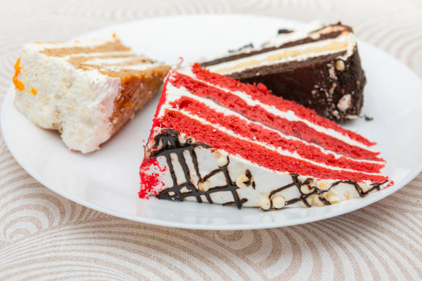 Cake slices on dish. Red velvet, Carrot and chocolate cake on a white dish. \nSheet food not so healthy, industrial cakes.