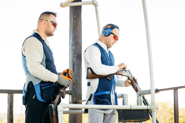 zwei erwachsene männer mit sonnenbrille, schützenden kopfhörern und einer gewehrweste, die das schießen mit feuerwaffen üben. - sport clipping path handgun pistol stock-fotos und bilder