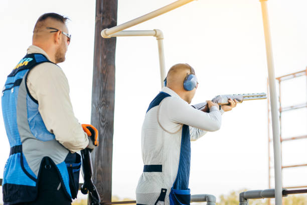 zwei erwachsene männer mit sonnenbrille, schützenden kopfhörern und einer gewehrweste, die das schießen mit feuerwaffen üben. - sport clipping path handgun pistol stock-fotos und bilder