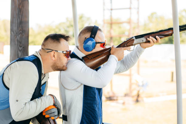 zwei erwachsene männer mit sonnenbrille, schützenden kopfhörern und einer gewehrweste, die das schießen mit feuerwaffen üben. - sport clipping path handgun pistol stock-fotos und bilder