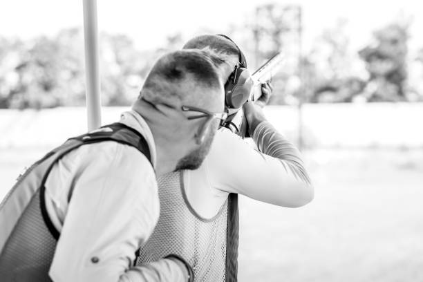 zwei erwachsene männer mit sonnenbrille, schützenden kopfhörern und einer gewehrweste, die das schießen mit feuerwaffen üben. - sport clipping path handgun pistol stock-fotos und bilder