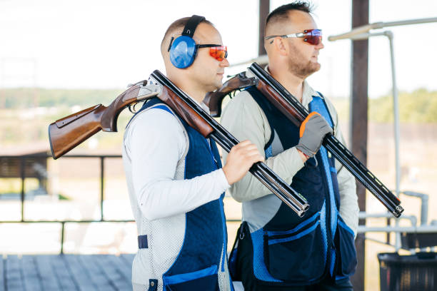 портреты двух взрослых мужчин в солнцезащитных очках, защитных наушниках и жилете, практикующих стрельбу из огнестрельного оружия. - rifle sport air target shooting стоковые фото и изображения
