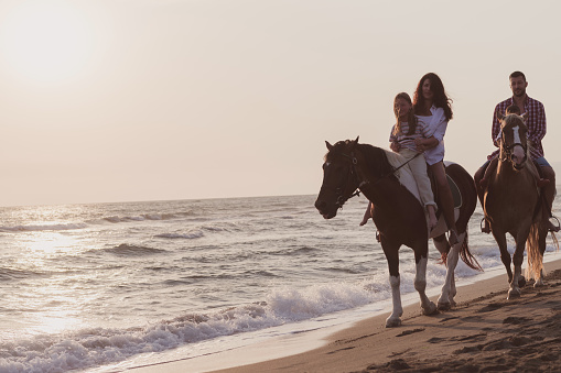 The family spends time with their children while riding horses together on a sandy beach. Selective focus. High quality photo
