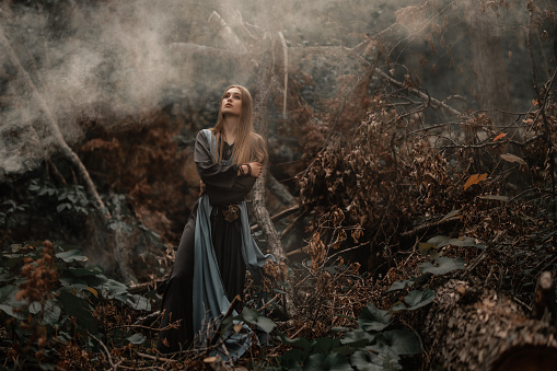 A mysterious witch dressed in a vintage costume walks in a dark forest