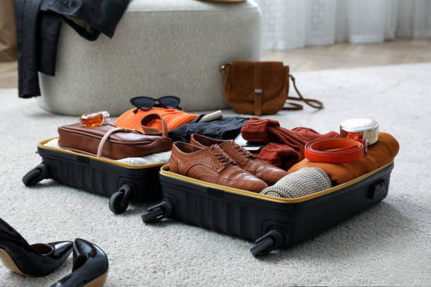 istock Open suitcase with folded clothes, accessories and shoes on floor indoors 1406891499