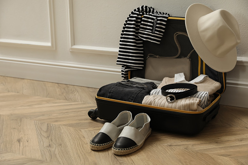 Open suitcase with folded clothes, accessories and shoes near white wall indoors, space for text