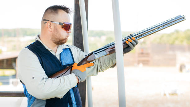 erwachsener mann mit sonnenbrille und gewehrweste, der das schießen mit feuerwaffen übt. junge erfahrene männliche zielschrotflinte im freien. - sport clipping path handgun pistol stock-fotos und bilder