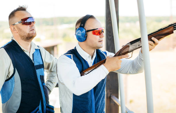 zwei erwachsene männer mit sonnenbrille, schützenden kopfhörern und einer gewehrweste, die das schießen mit feuerwaffen üben. - sport clipping path handgun pistol stock-fotos und bilder