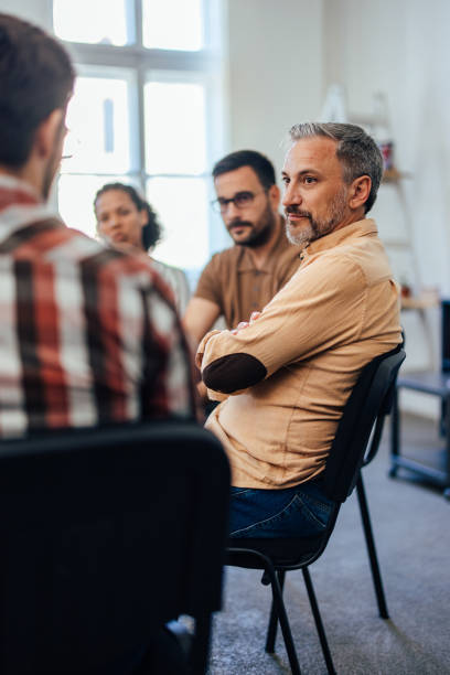 A focused man attends group therapy, being calm and listening to others. stock photo